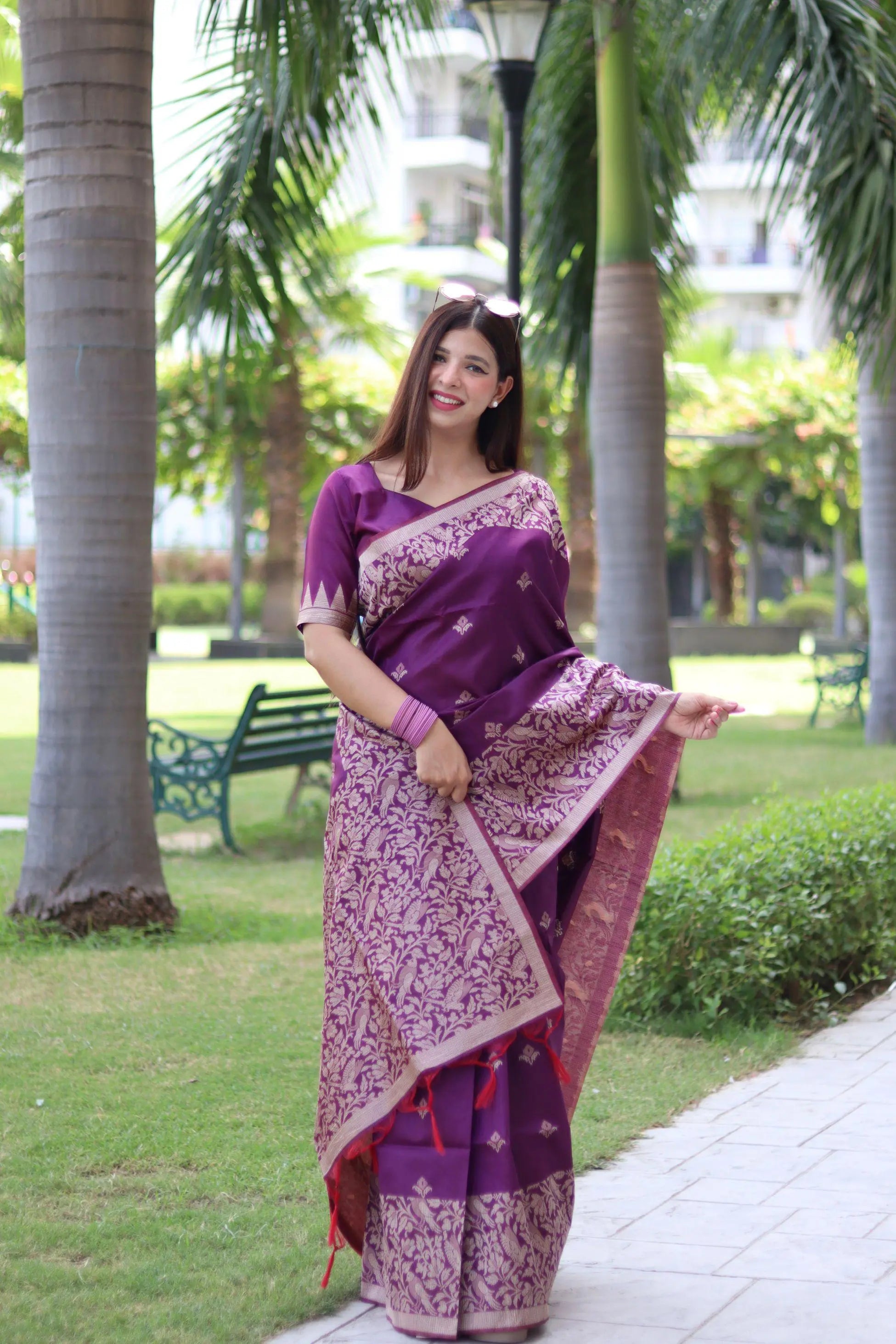 Woman wearing deep shade purple traditional weaving saree posing gracefully in a lush outdoor setting